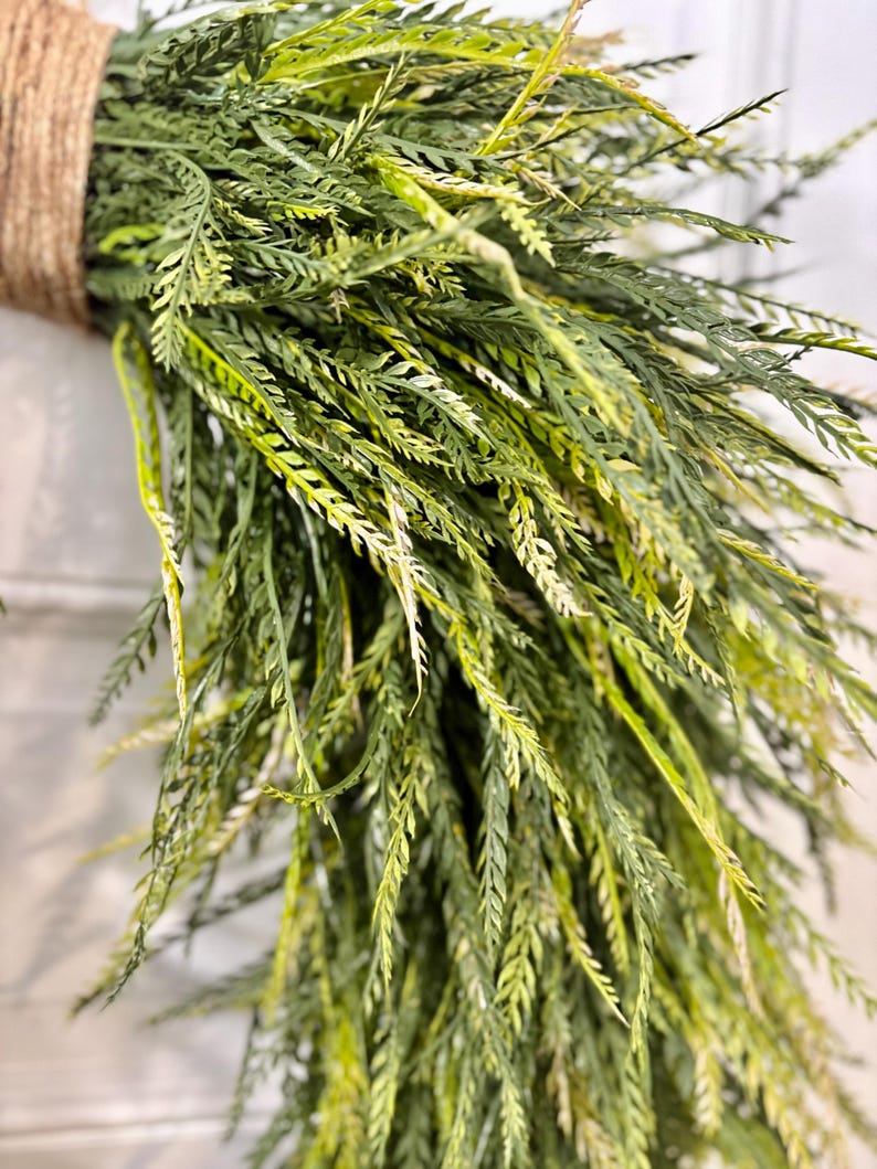 K&ouml;nnte beinhalten: Nahaufnahme eines B&uuml;ndels k&uuml;nstlichen Gr&uuml;ns, mit langen, schlanken Bl&auml;ttern in Gr&uuml;n- und Gelbt&ouml;nen. Die Bl&auml;tter sind mit einem dicken, naturfarbenen Bindfaden zusammengebunden, wodurch ein rustikales und strukturiertes Aussehen entsteht. Ideal f&uuml;r die Heimdekoration.
