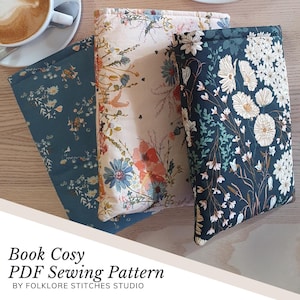 May include: Three book cozy sewing patterns with floral designs. The patterns are in shades of blue, cream, and pink. The text on the image reads "Book Cozy PDF Sewing Pattern by Folklore Stitches Studio".