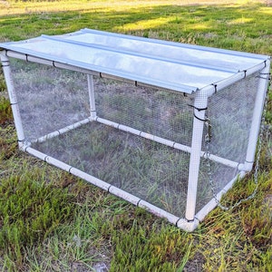 May include: A white PVC pipe frame covered in white mesh netting with a white plastic roof. The frame is secured with a chain.