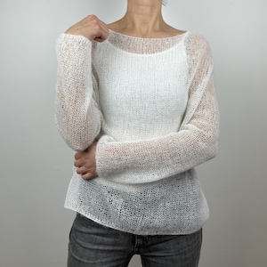 May include: A white, sheer knit sweater with a boat neck and long sleeves. The sweater has a loose, airy weave, creating a delicate, see-through effect. The garment is lightweight and appears to be made of a soft, possibly natural fiber. The style is casual and relaxed.