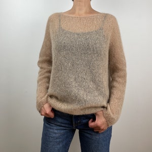 Könnte beinhalten: Ein hellbrauner, halbtransparenter Strickpullover mit lockerer Passform und langen Ärmeln. Der Pullover ist aus einem weichen, zarten Garn gefertigt und hat einen lässigen, entspannten Stil.