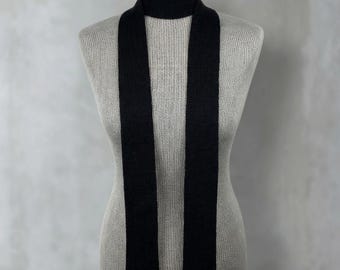 May include: A long, narrow black scarf with a ribbed knit texture. The scarf is wrapped around the neck of a mannequin, with two straight, vertical ends hanging down the front, creating a clean and simple look with a consistent dark color.