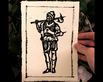 May include: Black and white woodcut print of a soldier wearing armor and holding a weapon. The soldier is standing with one leg slightly forward and is looking to the left. The print is on a white background.