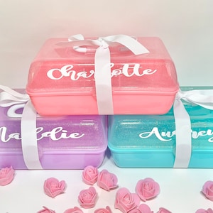 May include: Three colorful, glitter-covered boxes, each with a name in white script: Charlotte, Maddie, and Aubrey. Each box is tied with a white ribbon. Pink foam roses are scattered around the boxes.