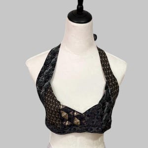 Könnte beinhalten: Ein Neckholder-Top mit einzigartigem Design, auf einer Schaufensterpuppe präsentiert. Das Top weist eine Mischung aus Mustern und Texturen in Schwarz-, Grau- und Brauntönen auf. Die Neckholder-Träger und das Oberteil haben verschiedene geometrische und strukturierte Muster.