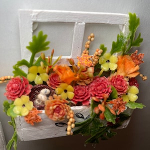 May include: A white window box planter filled with a variety of artificial flowers in shades of orange, red, and yellow. The flowers are arranged in a cascading style, with some flowers spilling over the edges of the box.