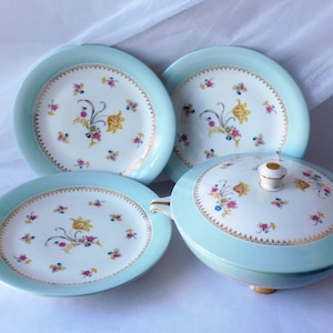 Puede incluir: Un juego de cuatro platos de porcelana vintage y una fuente cubierta con un borde azul claro y un patrón floral. Los platos y la fuente presentan un delicado diseño floral con flores amarillas, rosas y azules.