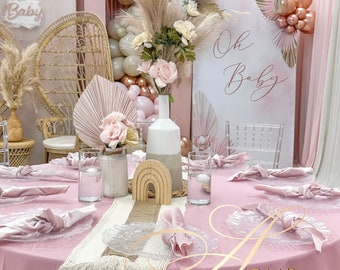 May include: A beautifully decorated baby shower scene with a pink color scheme. The table is set with pink linens, clear plates, and napkins. Decorations include floral arrangements, balloons, and a sign that says "Oh Baby."