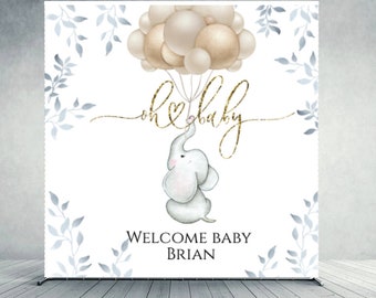 May include: A white baby shower backdrop with a gray elephant holding gold balloons that say "oh baby". The backdrop also has blue leaves and the text "Welcome Baby Brian".