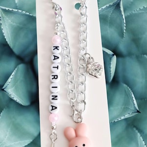 May include: A silver chain bracelet with a pink bunny charm and a beaded name charm that says "KATRINA".