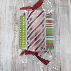 May include: Three wrapped gift tubes with red, white, and green striped paper. The tubes are tied together with a red ribbon with glitter.