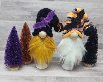 May include: Three Halloween gnomes with black, white, and yellow beards. The gnomes are wearing black and orange striped hats with a black bat on top. The gnomes are standing on a wooden surface.
