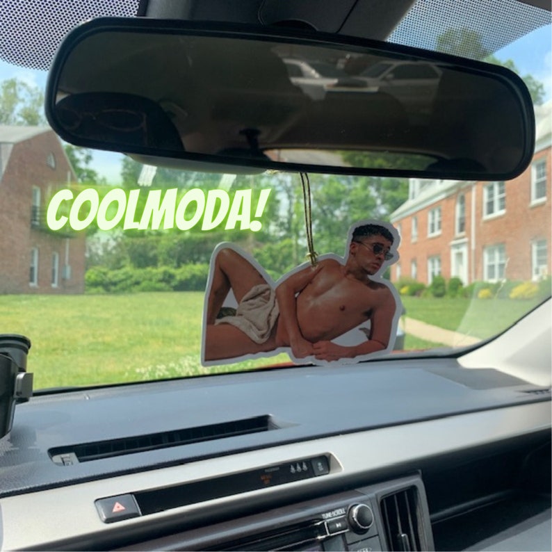 Op de afbeelding: Een autoluchtverfrisser met een foto van een man in een witte handdoek. De luchtverfrisser hangt aan de achteruitkijkspiegel. De tekst "COOLMODA!" is zichtbaar in de afbeelding.