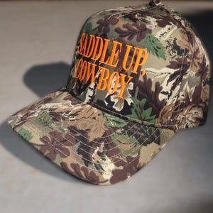camo trucker hat, hat cowboy snapback, snapback cap country, country western cap, cap woodland hunting, hunting headwear orange, orange embroidered hat, hat rodeo style, style rustic hunting, hunting camouflage baseball, baseball hat outdoor, outdoor ranch accessory, saddle up cowboy