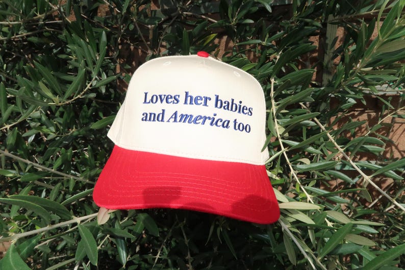 embroidered canvas cream and red hat in royal blue thread that says Loves her babies and America too