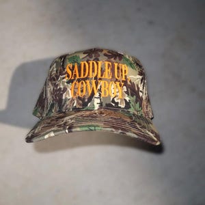 camo trucker hat, hat cowboy snapback, snapback cap country, country western cap, cap woodland hunting, hunting headwear orange, orange embroidered hat, hat rodeo style, style rustic hunting, hunting camouflage baseball, baseball hat outdoor, outdoor ranch accessory, saddle up cowboy