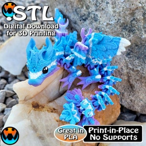 May include: A blue and white 3D printed dragon figurine with purple accents. The dragon is posed on a rock with the text "STL Digital Download for 3D Printing" and "Great in PLA Print-in-Place No Supports" below it.