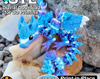 May include: A blue and white 3D printed dragon figurine with purple accents. The dragon is posed on a rock with the text "STL Digital Download for 3D Printing" and "Great in PLA Print-in-Place No Supports" below it.