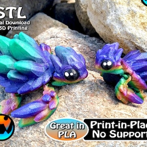 Op de afbeelding: Twee 3D-geprinte, kleurrijke, kristalachtige wezens met grote ogen. De wezens zijn voornamelijk blauw, paars en groen, met regenboogaccenten. De afbeelding bevat tekst die luidt ".STL Digital Download for 3D Printing" en "Great in PLA Print-in-Place No Supports."