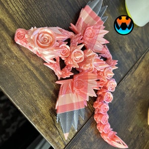 Pu&ograve; includere: Una statuetta di drago stampata in 3D rosa e nera con dettagli di rose. Il drago ha ali, una coda e una testa con una rosa sul naso.