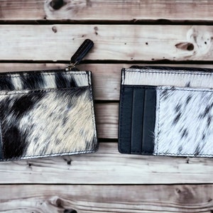May include: Two black and white cowhide leather card holders with a zipper closure. The card holders have multiple card slots and are made of a soft, supple leather.