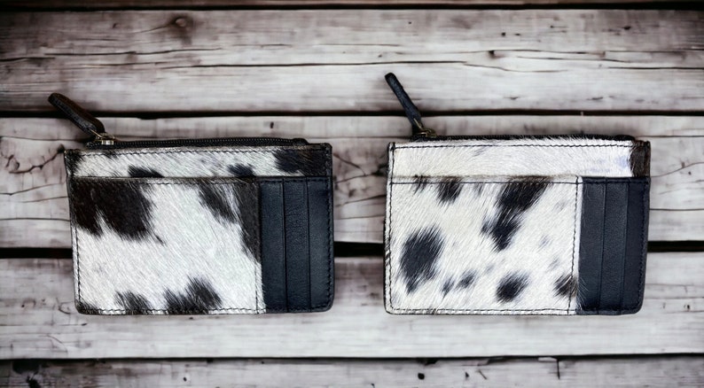 May include: Two black and white cowhide leather wallets with a zipper closure and a black leather card slot.
