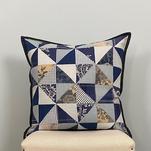 Peut inclure: Un oreiller bleu et beige en patchwork avec un motif géométrique. L'oreiller a une bordure noire et est fait de différents tissus.