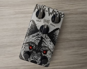 Puede incluir: Un pedal de guitarra plateado con un gráfico de lobo en blanco y negro y el texto "Aul-Woo-oo" y "Sketchy Sounds". El pedal tiene perillas etiquetadas como "Howl", "Growl", "Bite" y "Octave".