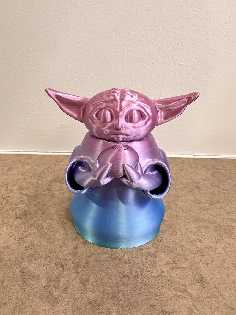 K&ouml;nnte beinhalten: Eine 3D-gedruckte Figur eines beliebten Charakters aus dem Star Wars-Franchise. Die Figur h&auml;lt eine kleine Kugel in ihren H&auml;nden. Die Figur ist in einem Farbverlauf von Pink und Blau bemalt.