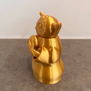 K&ouml;nnte beinhalten: Eine goldfarbene 3D-gedruckte Figur eines beliebten fiktiven Charakters. Die Figur h&auml;lt ein kleines Objekt in ihren H&auml;nden.
