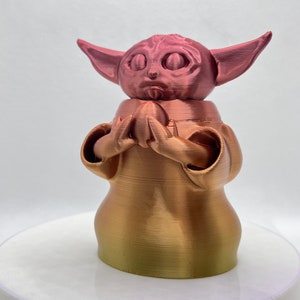 K&ouml;nnte beinhalten: Eine 3D-gedruckte Figur eines beliebten Charakters aus dem Star Wars-Franchise. Die Figur ist aus einem Farbverlaufsmaterial gefertigt, das von einer Ros&eacute;goldfarbe zu einer Goldfarbe &uuml;bergeht. Die Figur h&auml;lt ein kleines Objekt in ihren H&auml;nden.