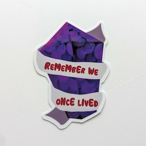 May include: Purple gemstone sticker with a white banner that reads "Remember we once lived".