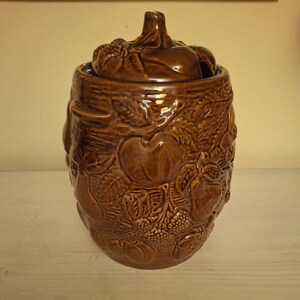 Puede incluir: Un tarro de cerámica marrón con tapa, decorado con un diseño en relieve de frutas y hojas.