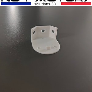 Może przedstawiać: Biały plastikowy narożnik z czterema otworami montażowymi. Narożnik ma zaokrąglony brzeg i mały rant na dole.
