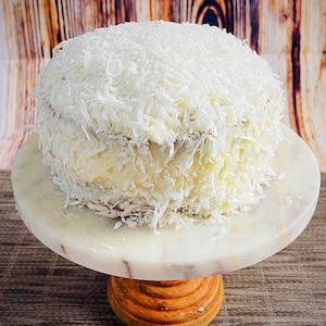 May include: A white cake frosted with white frosting and covered in shredded coconut.