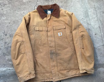 May include: A tan work jacket with a brown corduroy collar. The jacket has two chest pockets, two lower pockets, and a small logo patch. The jacket is made of a durable material and is designed for work.