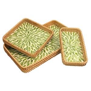 May include: Four woven rattan trays of varying sizes. The trays have a square or rectangular shape with a light beige background and a green leaf pattern. The edges of the trays are a natural brown color.