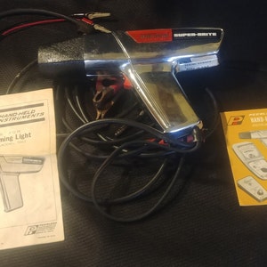 May include: A vintage Peerless Super-Brite power timing light with a chrome finish, black cable, and red and black connectors. Includes two instruction manuals. Automotive test equipment.