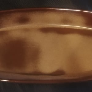 May include: A rectangular, brown ceramic serving dish with rounded corners. The dish has a glossy finish and a slightly textured surface. The color is a warm, earthy tone, suitable for serving appetizers or small dishes.