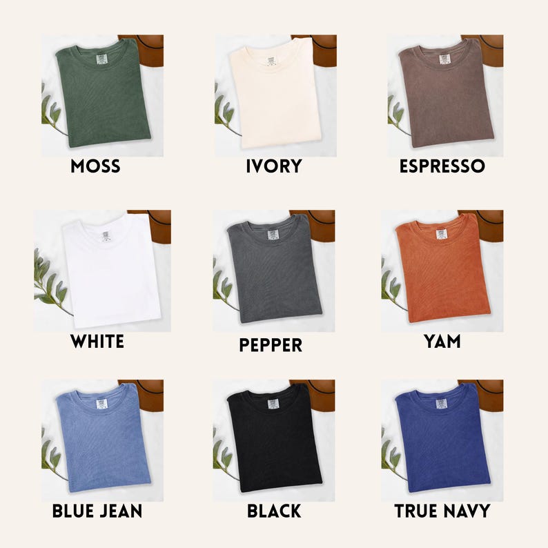 Op de afbeelding: Negen verschillend gekleurde t-shirts worden getoond, elk netjes opgevouwen. Kleuren zijn onder meer mos, ivoor, espresso, wit, peper, yam, spijkerbroekblauw, zwart en marineblauw. Elk shirt heeft een label en is op een neutrale achtergrond geplaatst.