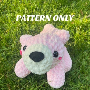 May include: A pink crocheted plush bear with white fur around the nose and black eyes. The bear is sitting on a bed of green grass. The text "PATTERN ONLY" is written in white letters on a green background above the bear. The text "*NOT a physical plushie" is written in white letters on a green background below the bear.