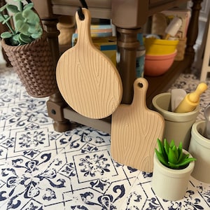 May include: Two wooden cutting boards, one round and one rectangular, with a wood grain pattern. The boards are hanging on a wooden shelf.