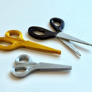 May include: Three pairs of scissors in gold, black and silver. The scissors are arranged on a white surface. The scissors have a loop handle and pointed blades. The scissors are likely for crafting or general use.