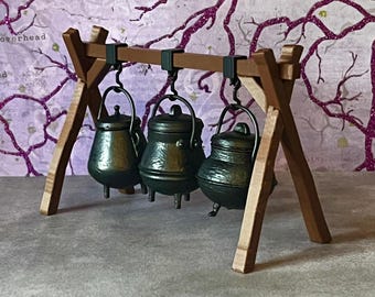 May include: Three black metal cauldrons hanging from a wooden tripod stand. The cauldrons have lids and are hanging from hooks on the stand.