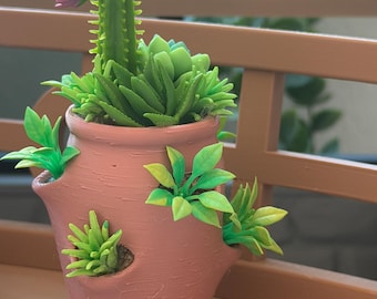 May include: A terracotta-colored, multi-tiered planter with several small openings along its sides. The planter is filled with various artificial green succulents and a single tall green cactus topped with a small, light purple flower bloom.