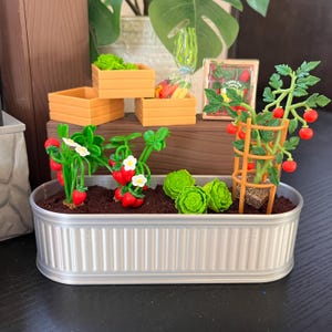 Könnte beinhalten: Eine Miniaturgartenszene mit einem verzinkten Metallpflanzer, der mit Erde und verschiedenen Pflanzen wie Erdbeeren und Tomaten gefüllt ist. Holzkisten enthalten Salat und andere Produkte. Ein kleines Schild trägt die Aufschrift "Happy Farm".