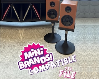 May include: Two miniature brown speakers with black circular drivers, each mounted on a black pedestal stand with a round base. The image includes the text MINI BRANDS! COMPATIBLE STL FILE in white and purple lettering on a pink starburst background.