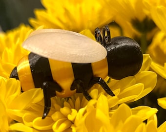 May include: A black and yellow bee figurine with a white plastic wing, perched on a yellow flower.