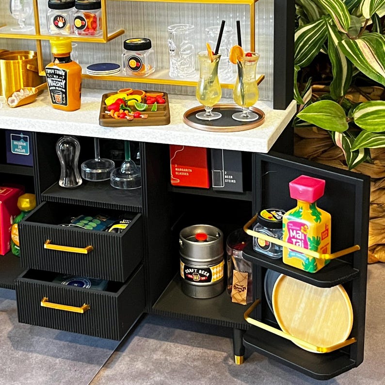 Op de afbeelding: Een zwarte barwagen met twee laden, een plank en een kast. De wagen heeft verschillende items erop, waaronder flessen sterke drank, glazen en een blikje ambachtelijk bier. De wagen is versierd met gouden accenten.