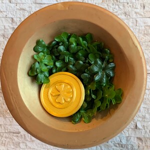 May include: A gold bowl filled with green shamrock leaves and a gold coin with a four-leaf clover design.